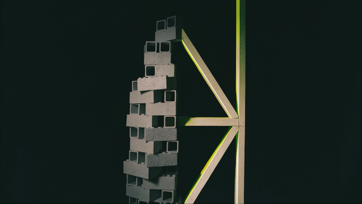 Stillleben-Kontrast: links ein wackliger Turm aus identischen grauen Bausteinen, rechts ein präzise gefügtes Holz-Fachwerk mit chartreuse-grüner Lichtkante — Sinnbild für Baukasten-Website und handwerklich gebaute Website.