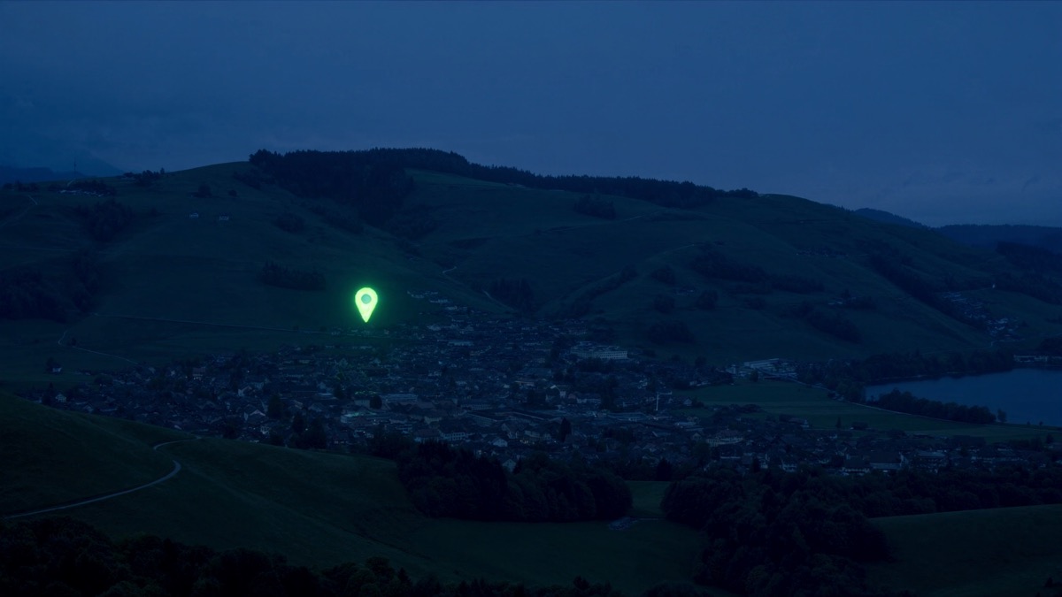 Ein einzelner leuchtend grüner Karten-Pin schwebt in der blauen Stunde über einer Schweizer Gemeinde zwischen See und Hügeln und markiert das Ziel von Local SEO: die lokale Auffindbarkeit eines Betriebs.
