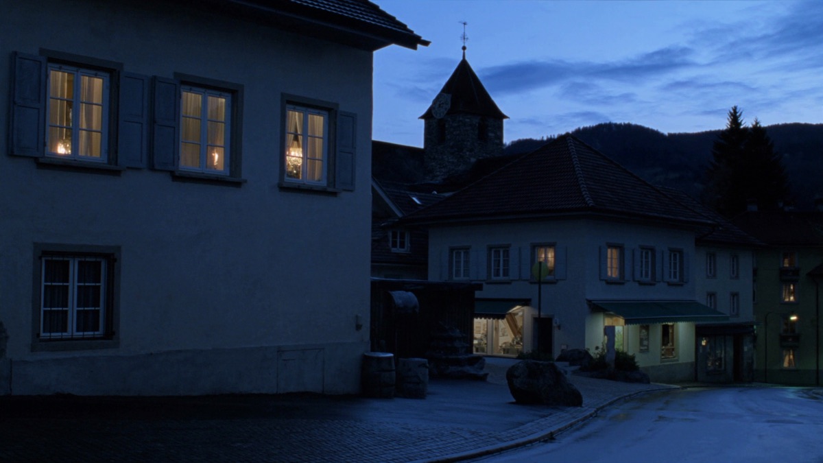Abendstimmung in einer Kleinstadt im Zürcher Oberland: warm erleuchtete Fenster, ein Kirchturm mit Uhr und bewaldete Hügel hinter den Dächern — Sinnbild für den Heimmarkt von Studio Erdinc.