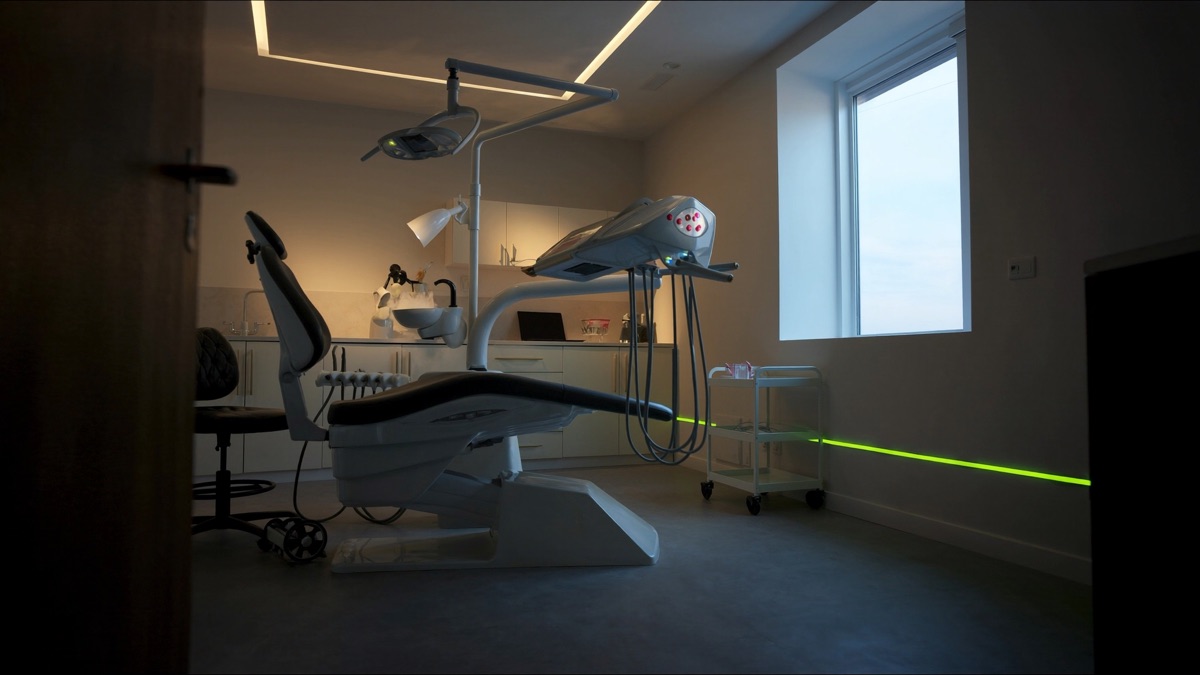 Menschenleeres, modernes Zahnarzt-Behandlungszimmer in der Abenddämmerung mit Behandlungsstuhl, OP-Leuchte, Abendlicht im Fenster und einer chartreuse-grünen LED-Lichtlinie an der Wand — Sinnbild für eine Zahnarzt-Website, die Patientinnen und Patienten wie auch KI-Antwortmaschinen erreicht.