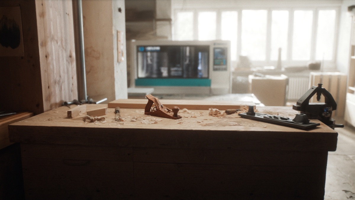 Helle Schreinerwerkstatt: Werkbank mit Handhobel, Stemmeisen und Holzspänen im Vordergrund, im Hintergrund eine moderne CNC-Fräsmaschine vor grossen Fenstern.